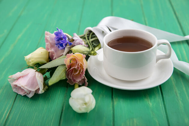 领带一杯茶的俯视图 可爱的花朵像雏菊玫瑰 用彩带系在绿色的木制背景上茶顶部杯子