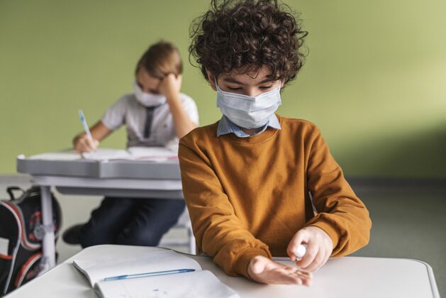 流行病带医用面罩的孩子在课堂上消毒手的正面图知识新常态水平