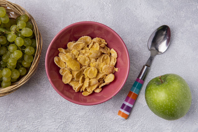 白色顶视图：碗里放着玉米片 茶匙里放着青苹果和白底绿葡萄绿色茶匙玉米片