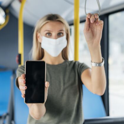 预防公交车上戴着医用面罩的女士举着智能手机的前视图流行病病毒女人