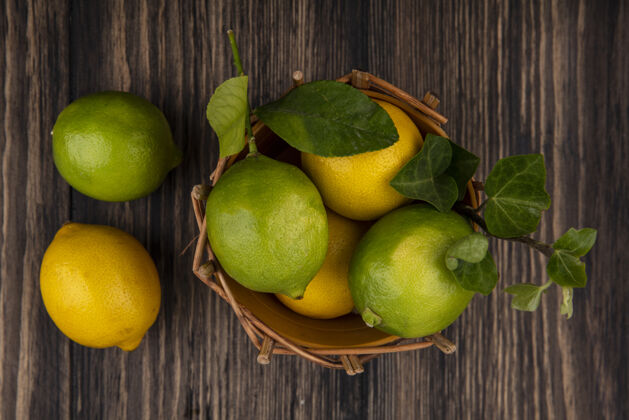 酸橙木制背景上的篮子里有柠檬的酸橙水果景观柑橘
