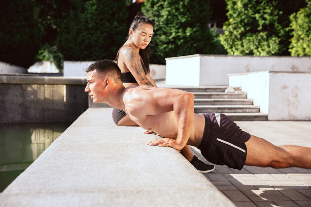 肌肉一个肌肉发达的运动员在公园里做运动体操 训练 健身 柔韧性锻炼夏日城市里阳光明媚的日子背景场积极健康的生活方式 青春 健美情侣肌肉活动