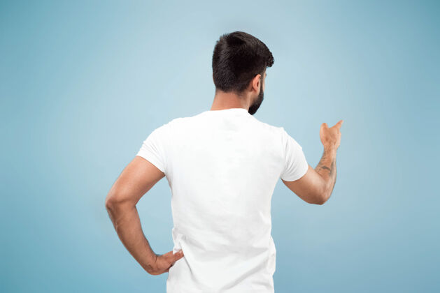 成人蓝色背景上穿着白衬衫的印度年轻人的半身特写肖像人类情感 面部表情 广告概念负面空间展示空酒吧 指向 选择 邀请胡须男人手势