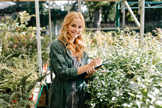 开花一位金发碧眼 笑容温柔的年轻女子 身着绿色长袍 系着腰带 正在温室里工作爱好花公园