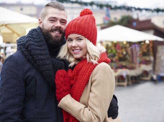 情侣在市场广场拥抱情侣牙齿微笑腰向上圣诞市场