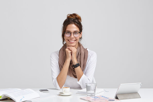 文书容貌开朗的记者 戴着透明眼镜 梳着黑发 边读书边丰富知识 带着温柔的微笑坐在工作台上用触摸板 一杯水商务女性学习平板电脑