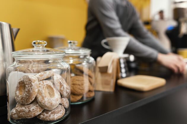 水平咖啡店柜台上放着饼干和点心 还有散焦的男咖啡师咖啡馆服务员雇员