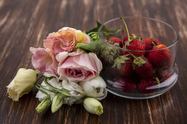 新鲜草莓在碗和木制背景上的花的侧视图水果食品花卉
