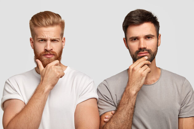 发型照片中严肃的两个男人抱着下巴 穿着休闲t恤 模特靠着白墙 陷入沉思 想办法解决问题姜男和他的朋友在室内摆姿势站剃胡子胡须