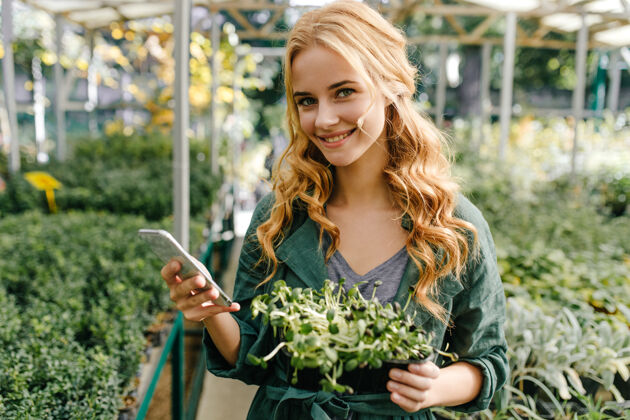 公园可爱的女孩 明亮的绿色眼睛 长长的卷发 心情很好温室里的肖像画上 漂亮的模特手里拿着电话和植物花情感金发