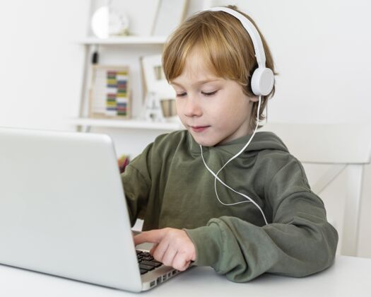 年轻人小男孩用带耳机的笔记本电脑耳机设备爱好