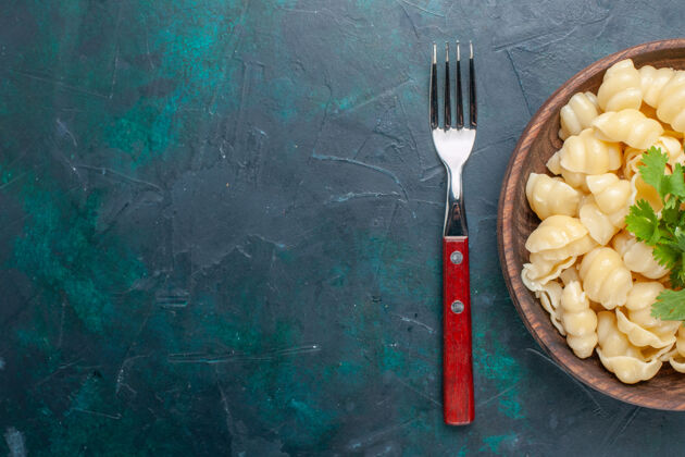 刀顶视图熟面团面食与绿色内板在深蓝色的桌子上饭菜叉子晚餐