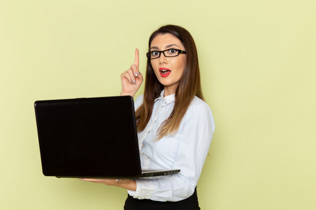 商务穿着白衬衫和黑裙子的女上班族正拿着笔记本电脑站在绿色的墙上拿着笔记本电脑办公室