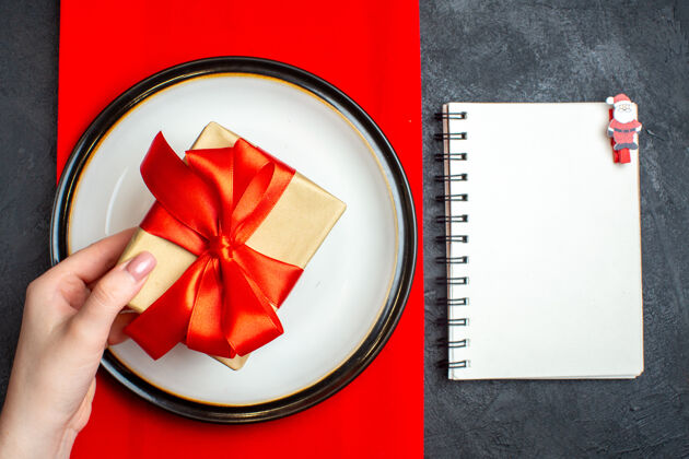 空盘子国家圣诞餐背景俯视图 手拿空盘子 红色餐巾上有蝴蝶结状的红丝带 黑色桌子上有笔记本视图餐巾国家