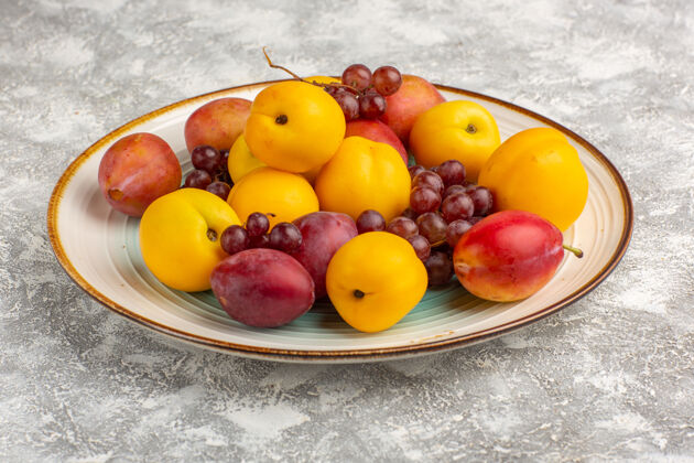 新鲜白色桌子上的盘子里放着新鲜甜美的杏子和李子和葡萄健康桃李子
