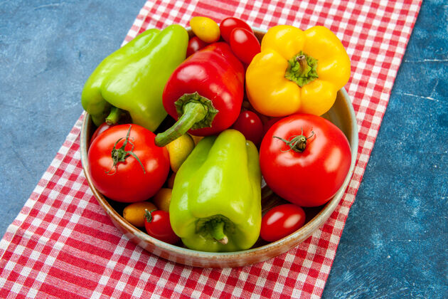 桌布顶视图新鲜蔬菜樱桃西红柿不同颜色甜椒西红柿孜然在盘子上红色和白色格子桌布在蓝色的桌子上蔬菜胡椒顶部