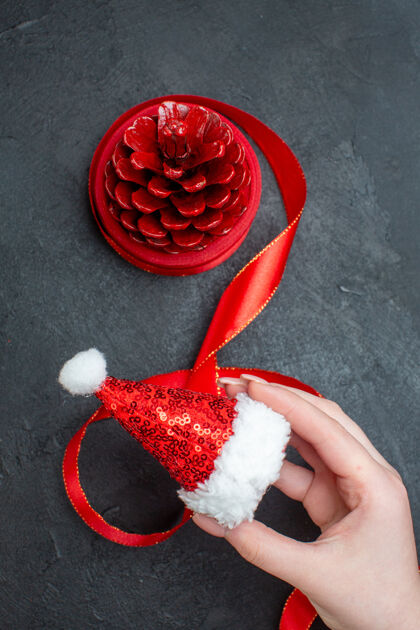 装饰手持圣诞老人帽和红色针叶树圆锥在黑暗背景下的垂直视图奶油圆锥形新鲜