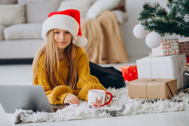 小小的可爱的女孩在圣诞树旁用电脑圣诞树美丽快乐的女人