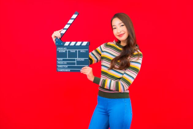 拍板在红色的隔离墙上用电影石板画出美丽的亚洲年轻女子电影板岩年轻人微笑