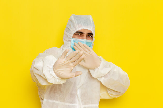 服装身着特殊防护服 戴着面具的男性科学工作者的正面图 摆在淡黄色的墙上科学灯防护