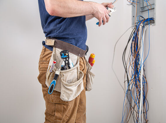 安装电工建筑工人在工作时 检查工业配电盘机身电线中的电缆连接专业人员穿着工作服 手持电工工具专业人员室内修理工