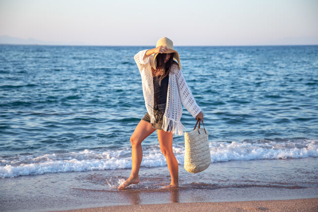 长廊一个戴着大帽子 挎着柳条袋的女孩走在海边暑假的概念帽子夏天海岸