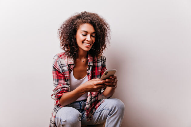 美国一个穿着格子衬衫的黑人女人正在用她的智能手机 一个正在读电话留言的迷人女孩时尚女人可爱