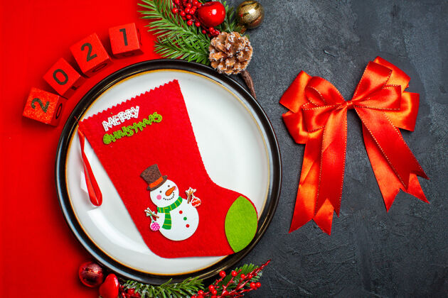 视图新年背景俯视图 圣诞袜子放在餐盘上 装饰配件杉木树枝和数字放在红餐巾上 红丝带放在黑桌子上容器树枝袜子
