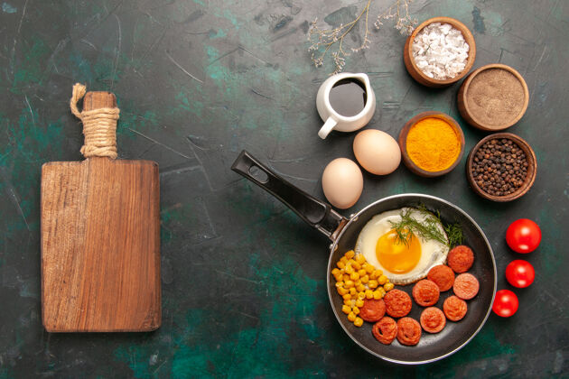 早餐在深绿色的背景上俯瞰炒鸡蛋 香肠和不同的调味品食品不同化妆品