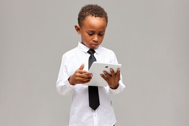 童年儿童与现代科技观念认真专注的美国黑人男生 身着制服 手持白色通用数字平板电脑 玩网络游戏或学习 有着集中的表达非洲游戏数码平板电脑