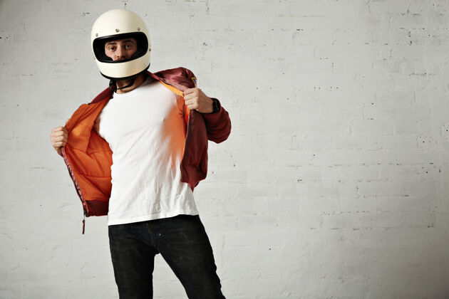男一个严肃的摩托车手穿着白色的复古头盔 展示着他紫红色夹克的橙色衬里休闲衣服帽子