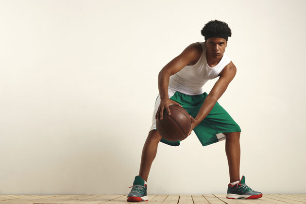 强壮严肃的黑人运动员 穿着绿白相间的衣服 膝盖上顶着一个老式篮球比赛动作篮球