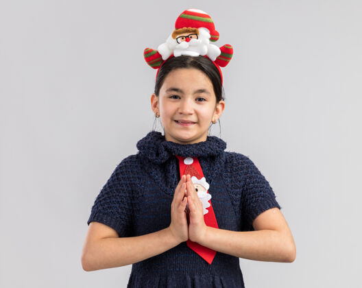 领带快乐的小女孩穿着针织连衣裙 头上系着一条红色的领带 头上戴着一个有趣的圣诞戒指 手拉着手 像是一个非常有趣的手势头圣诞节圣诞快乐