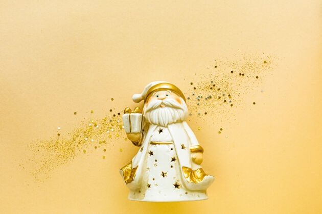 新的玩具圣诞老人用一个金色的礼品盒上的黄色背景假日概念 平放 俯视 复制空间花最小蜡烛
