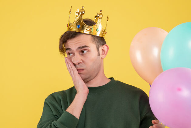 脸正面图失望的年轻人戴着皇冠拿着黄色的气球专业职业护目镜
