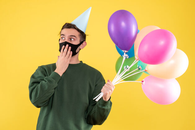 气球正面图：戴着派对帽 站在黄色地面上的彩色气球的年轻人帽子颜色生日