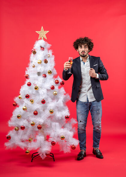 礼物在红色的白色圣诞树旁 站着一个留着胡子的年轻人 手里拿着酒庆祝新年男人圣诞庆祝