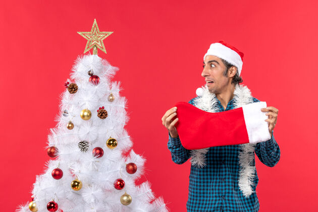 衬衫一个情绪化的年轻人 戴着圣诞老人的帽子 穿着蓝色的衬衫 手里拿着圣诞袜子男人侧面圣诞