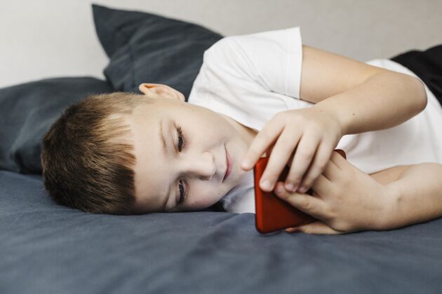 现代孩子躺在床上用手机侧视人数字设备房子