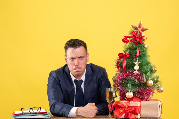 办公室沮丧的男人坐在圣诞树旁的桌子前 呈现黄色行政人员公司新郎