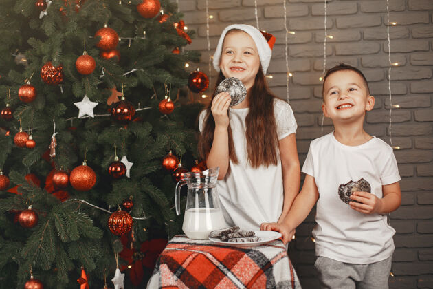 快乐站在圣诞树旁的孩子们吃牛奶饼干的孩子们小女儿节日