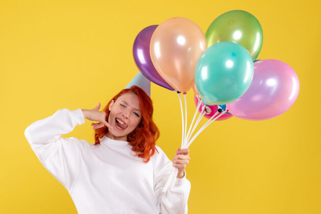 庆祝黄色墙壁上手持可爱彩色气球的年轻女子的正视图快乐气球礼物