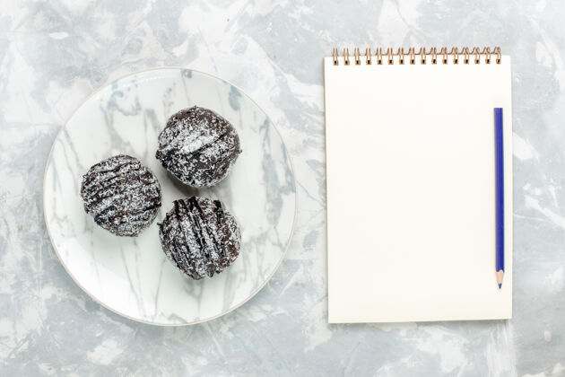 浅白色俯瞰美味的巧克力球圆形蛋糕加糖霜和笔记本在浅白的桌子上烤蛋糕巧克力糖派甜派蛋糕桌子
