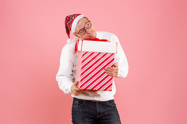 礼品盒粉红色墙上拿着大礼物的年轻人的正视图人举行十二月
