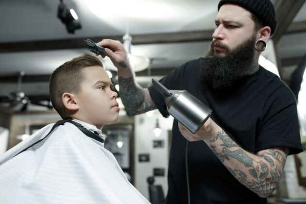 小伙子儿童理发师在黑暗中剪小男孩美容沙龙肖像