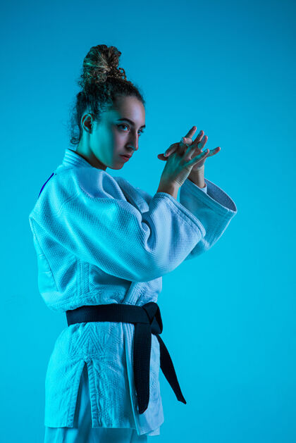 运动专业女柔道手穿着白色柔道和服 在蓝色neoned工作室背景下练习和训练黑色肌肉优雅