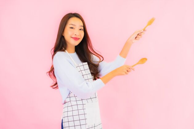 饮食肖像美丽的亚洲年轻女子在厨房穿着围裙在粉红色的隔离墙上美食微笑泰式