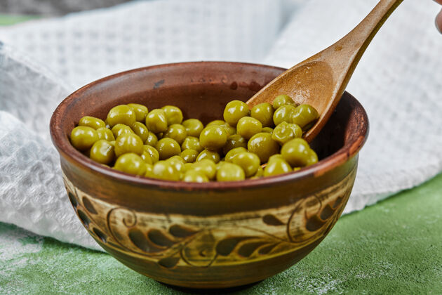 菜肴绿桌子上放着一碗煮青豌豆和一把木勺桌布木制食用