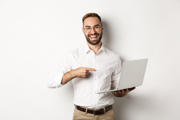 办公室商务部的帅哥经理戴着眼镜在笔记本上工作 指着电脑高兴地笑着 站着衬衫经理企业家