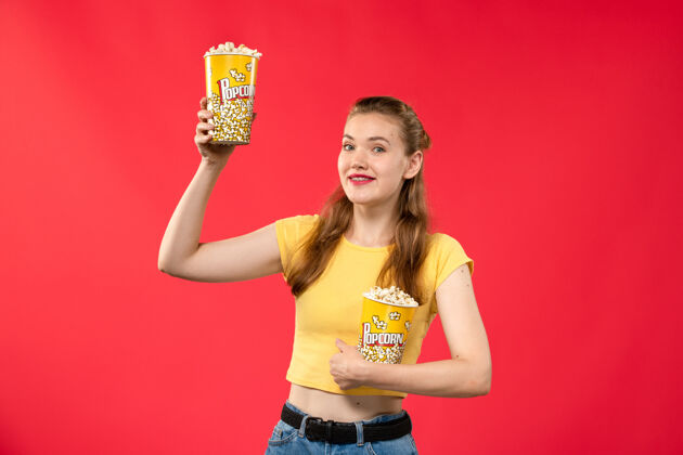 肖像正面图年轻的女性在电影院拿着爆米花在浅红色的墙上电影院女性欢乐时光电影爆米花浅红色剧院